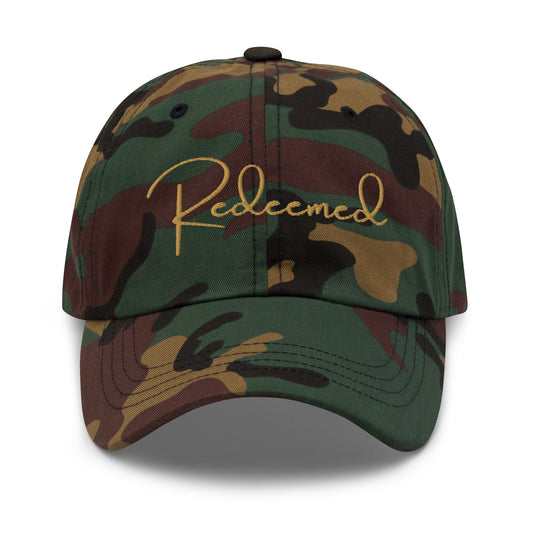 Front view of camo dad hat with “Redeemed” embroidered in gold script.