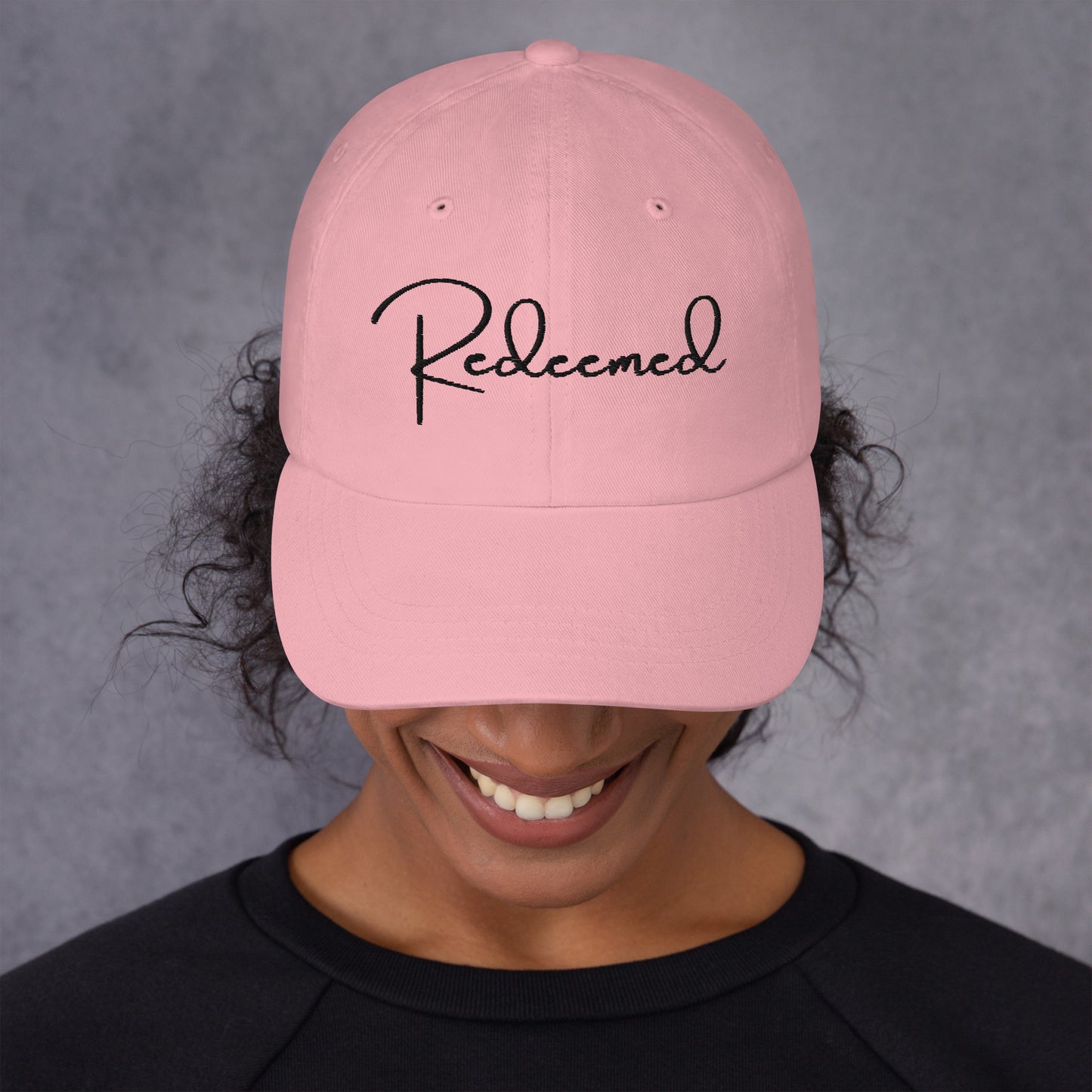 Front view of woman wearing pink dad hat with 'Redeemed' embroidered in black script