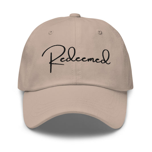 Front view of stone dad hat with 'Redeemed' embroidered in black script