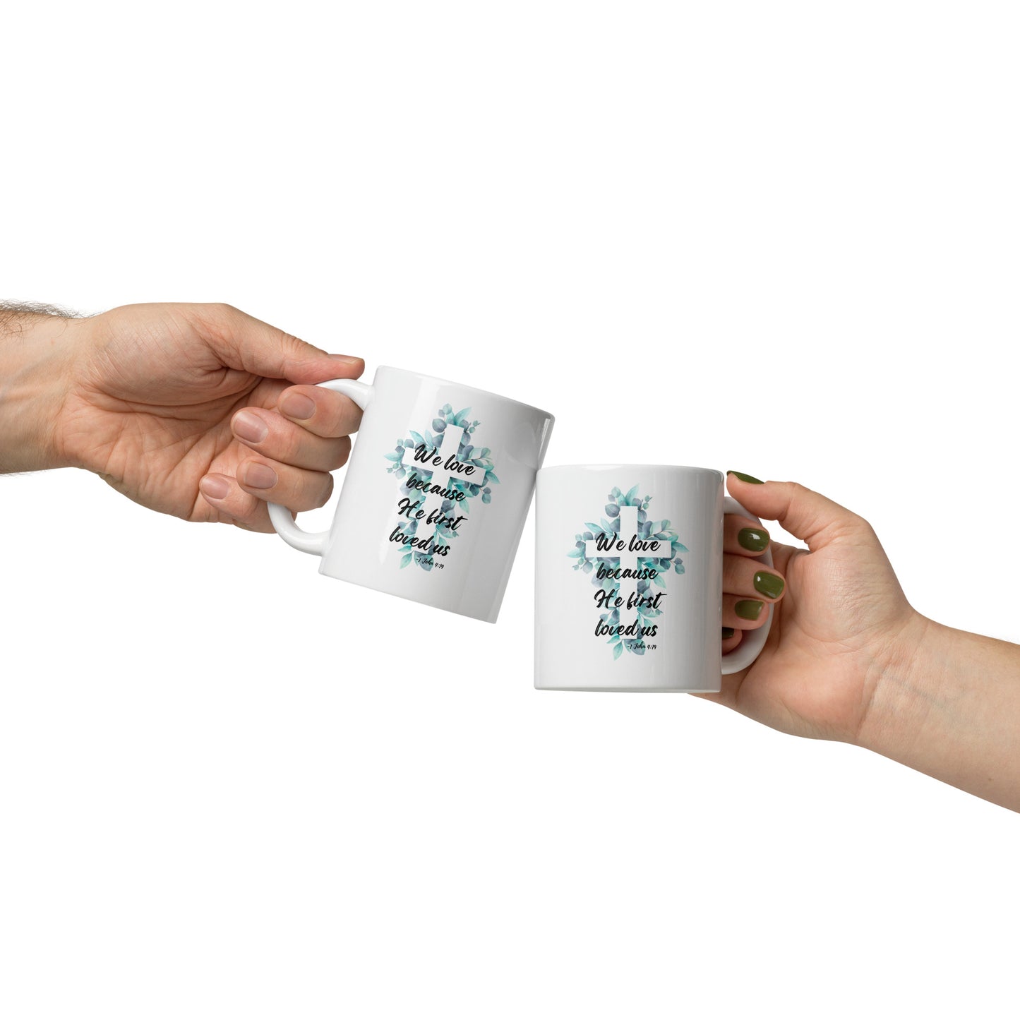 Two people clinking white 11oz ceramic mugs in a cheers gesture, each mug featuring a watercolor floral cross design inspired by 1 John 4:19.