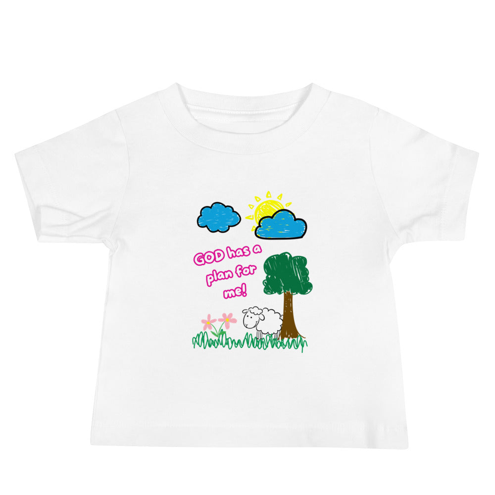 Front view of a baby girl wearing a light-colored Christian tee with pink text that says "God Has a Plan for Me" and a cheerful graphic showing a sheep in the grass with flowers, a tree, clouds, and sun.