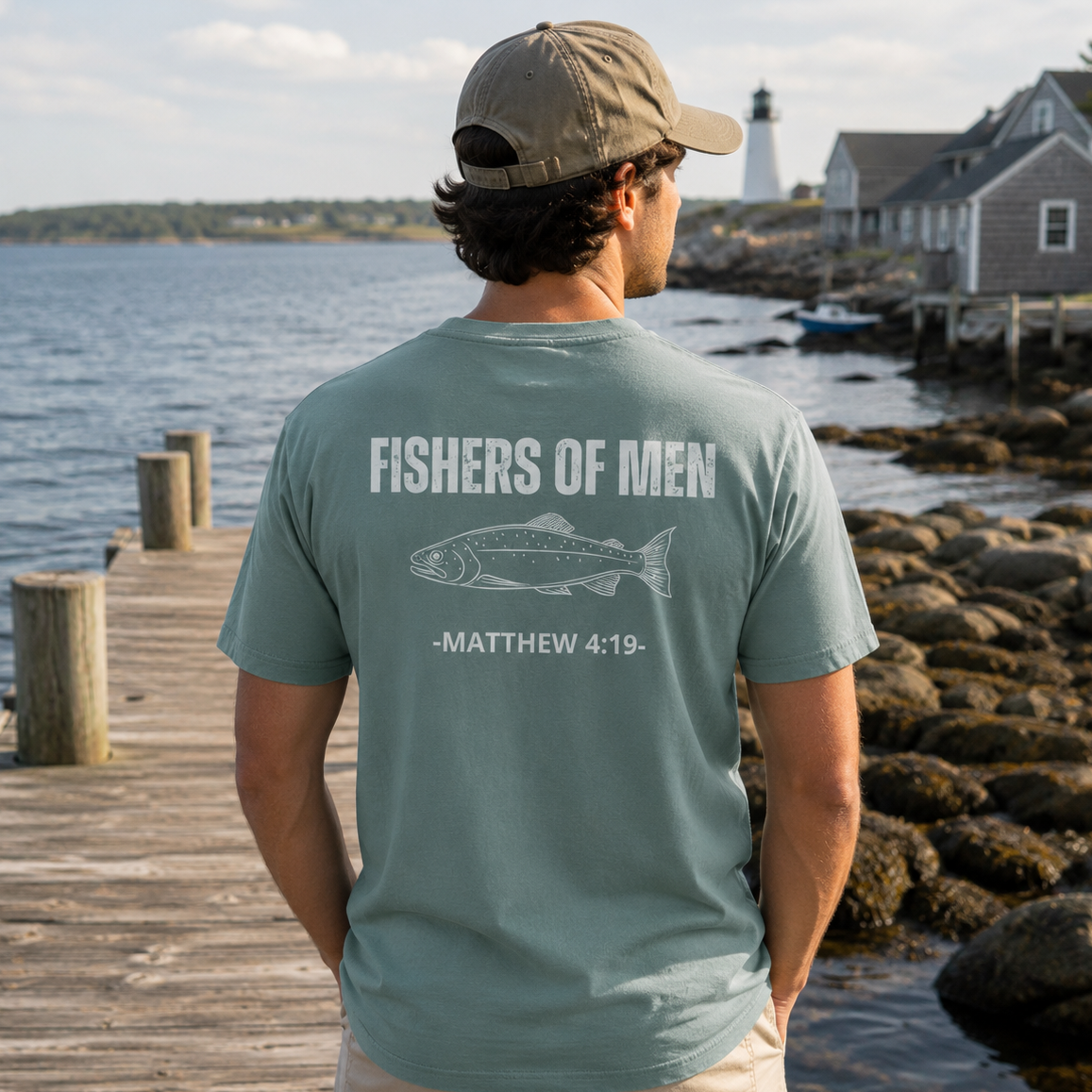 Man standing on a coastal dock wearing the Fishers of Men Tee in Green Bay featuring a fish graphic and Matthew 4:19 on the back.