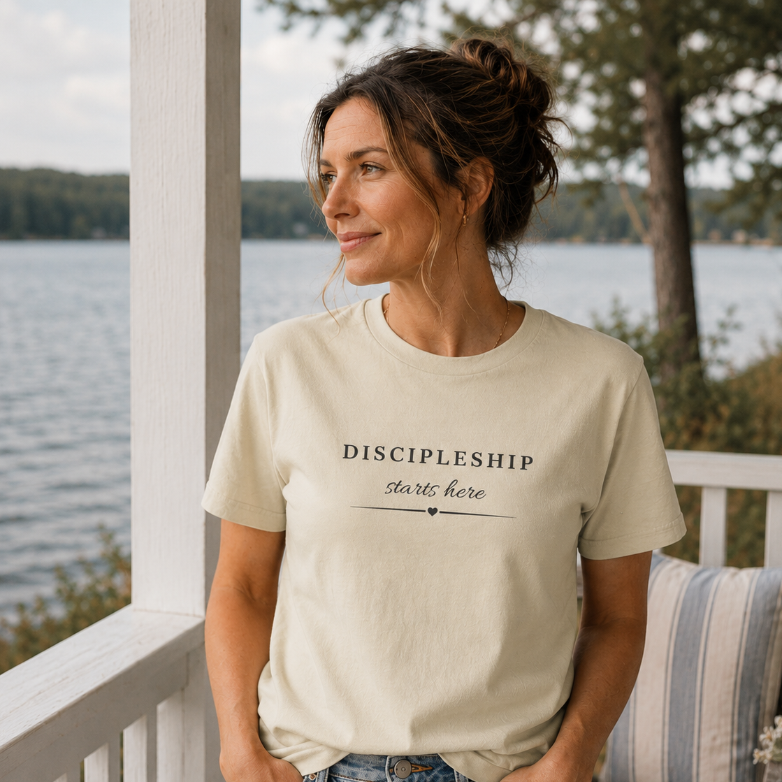 Woman wearing the Discipleship Starts Here Tee in Dyed Stone featuring the Discipleship Starts Here front design while overlooking the lake.