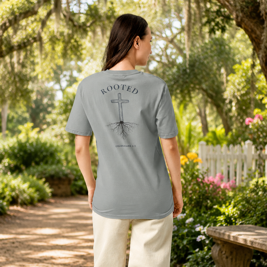 Woman wearing the Rooted in Christ Christian t-shirt in Misty Grey featuring a large cross and roots graphic with Colossians 2:7 on the back, photographed outdoors in a summer setting.