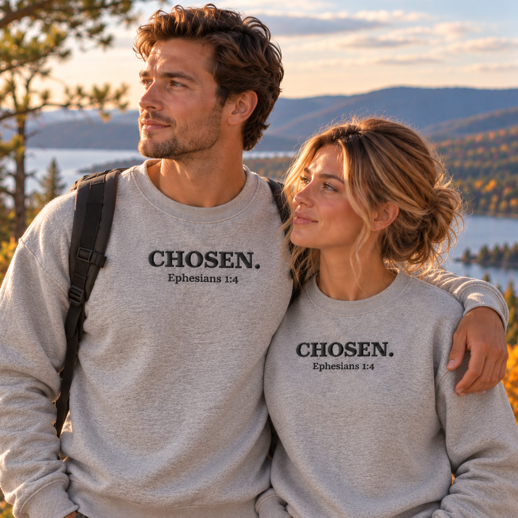 A man and a woman standing outdoors on a mountain overlook, both wearing light heather gray crewneck sweatshirts with the text 'CHOSEN. Ephesians 3:14' printed in black across the chest.
