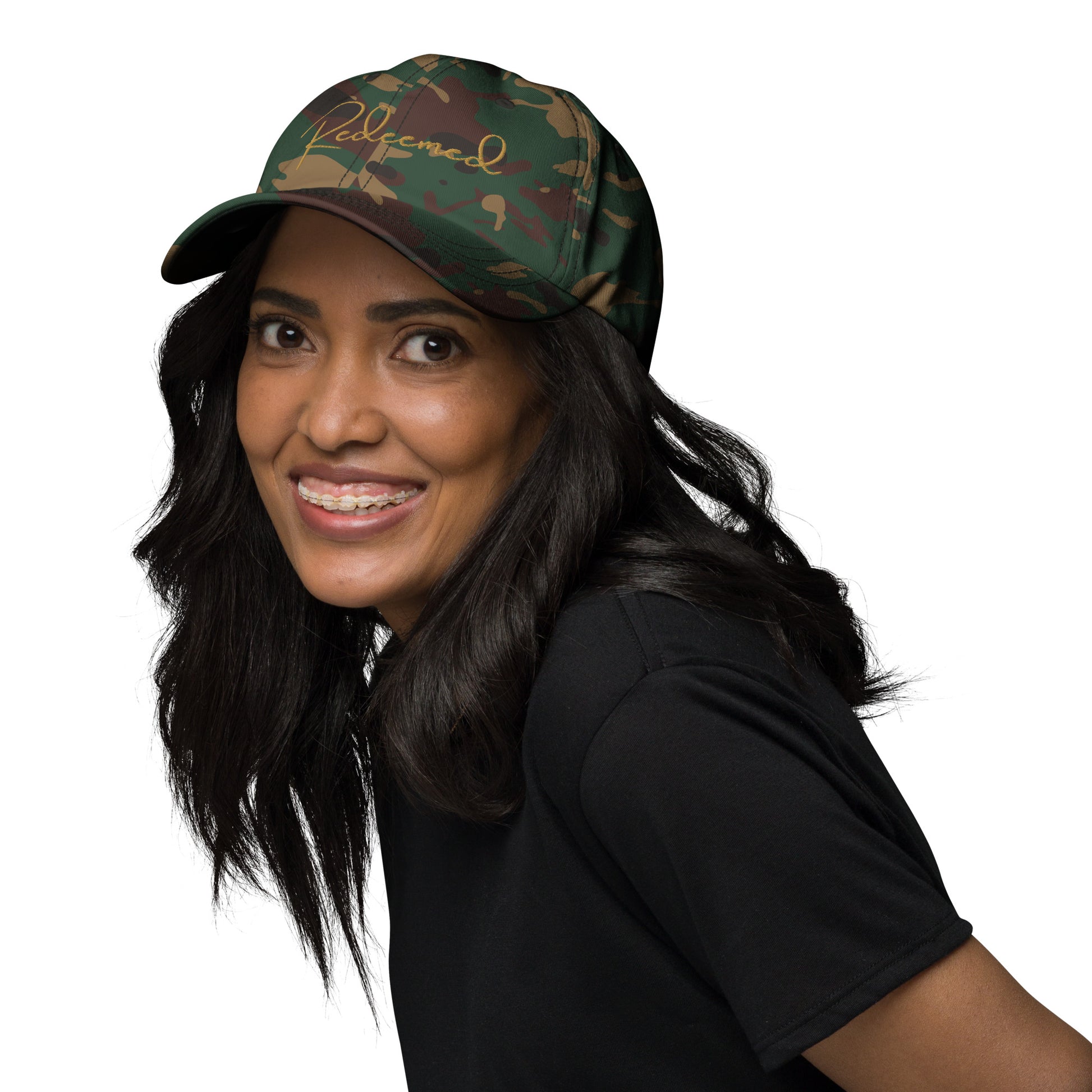 Smiling woman wearing camo Redeemed hat, styled with casual faith-based outfit.