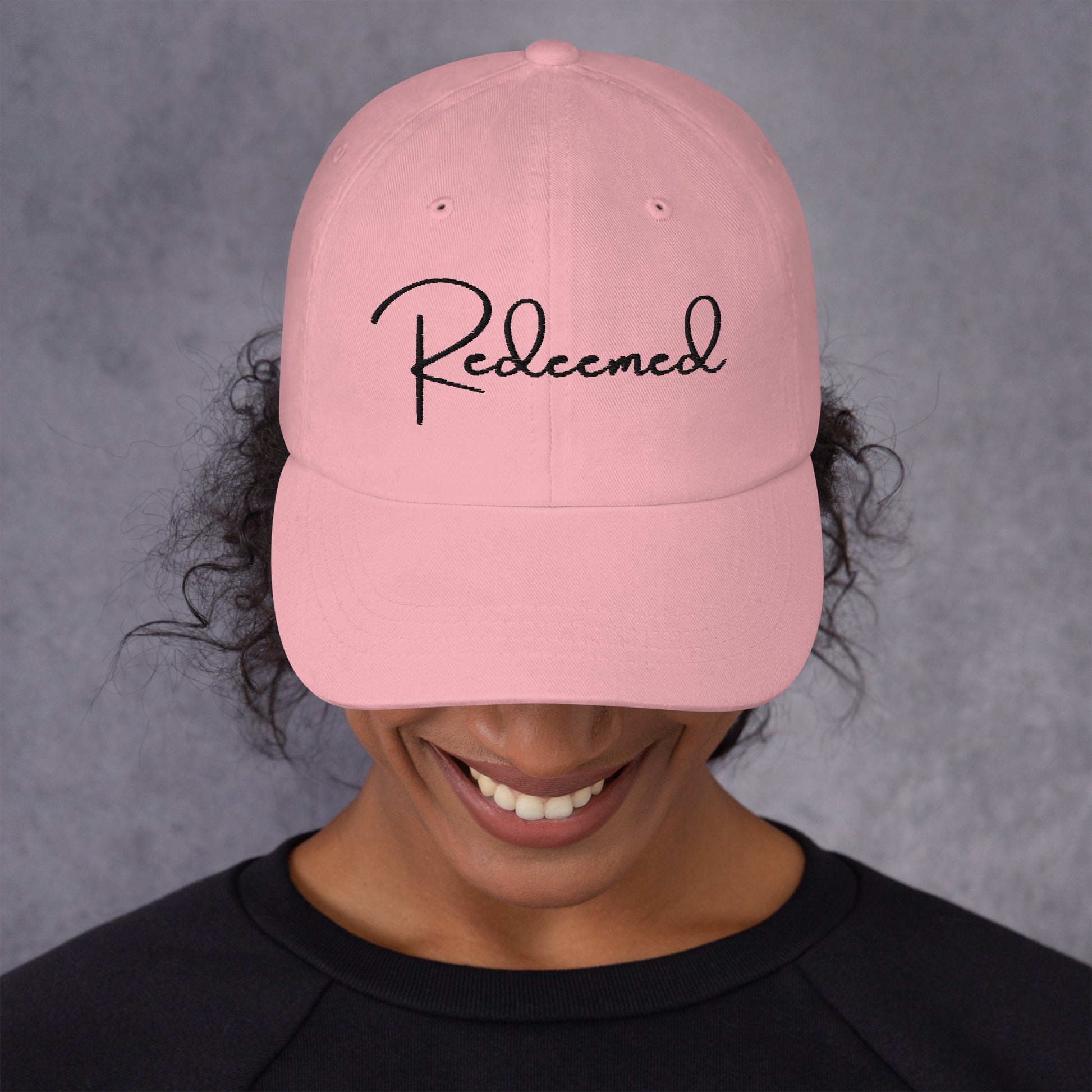 Front view of woman wearing pink dad hat with 'Redeemed' embroidered in black script