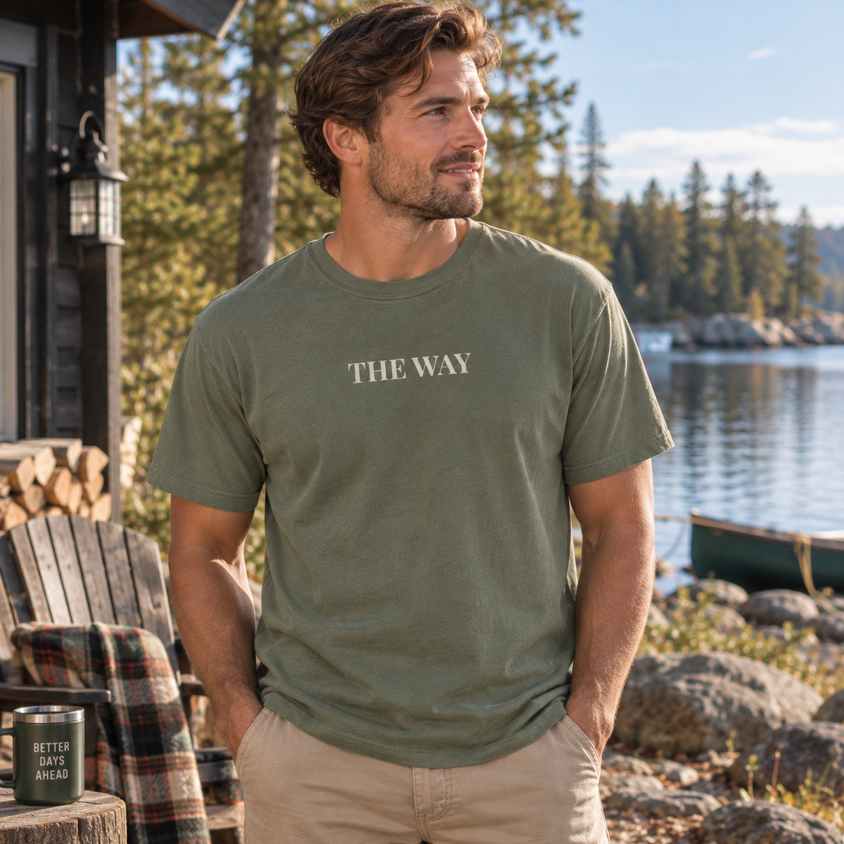 A man wearing a moss green t-shirt with the text 'THE WAY' printed in beige on the chest, standing outdoors near a lake and trees.
