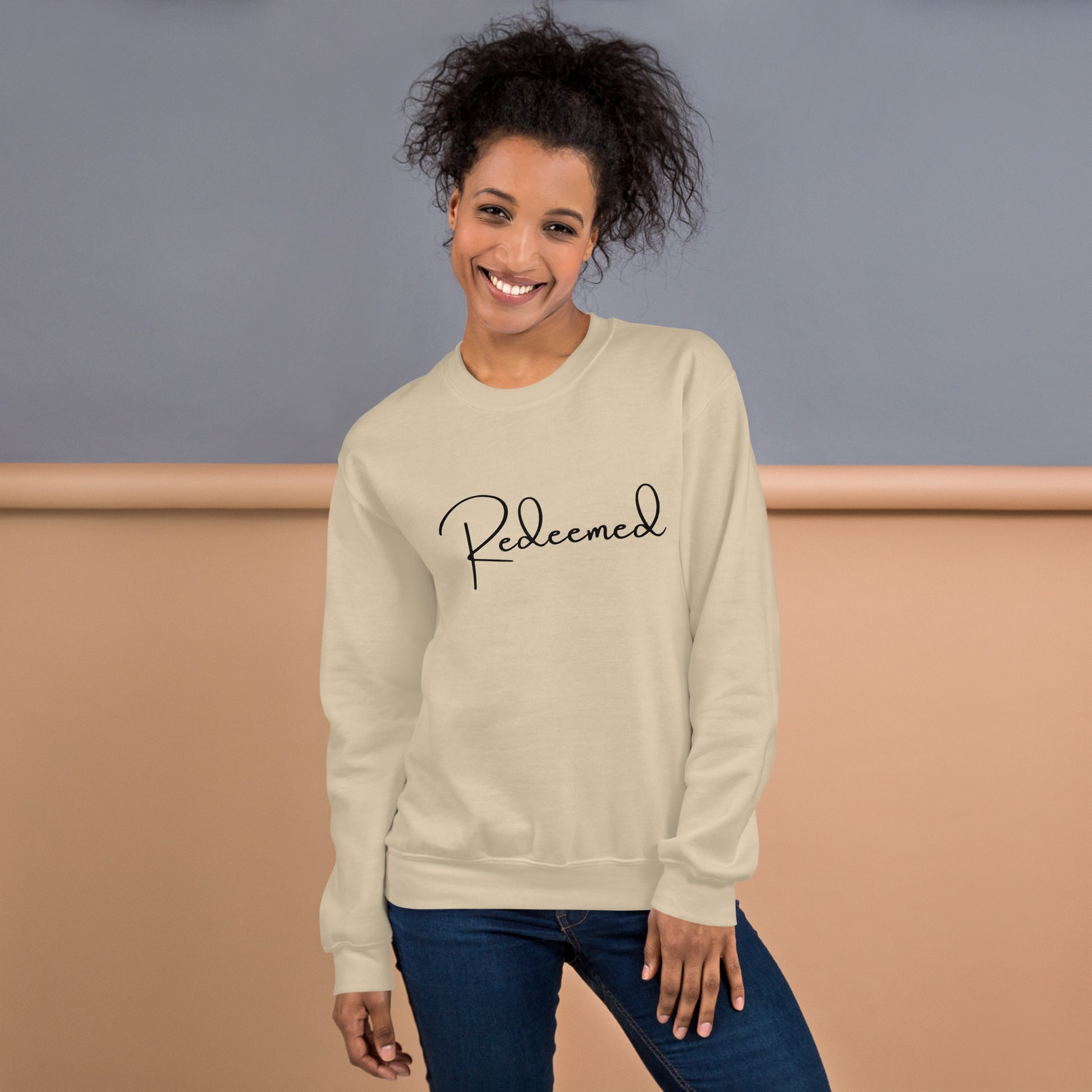 Female model wearing the Redeemed crewneck in Sand, front-facing lifestyle shot in natural setting.