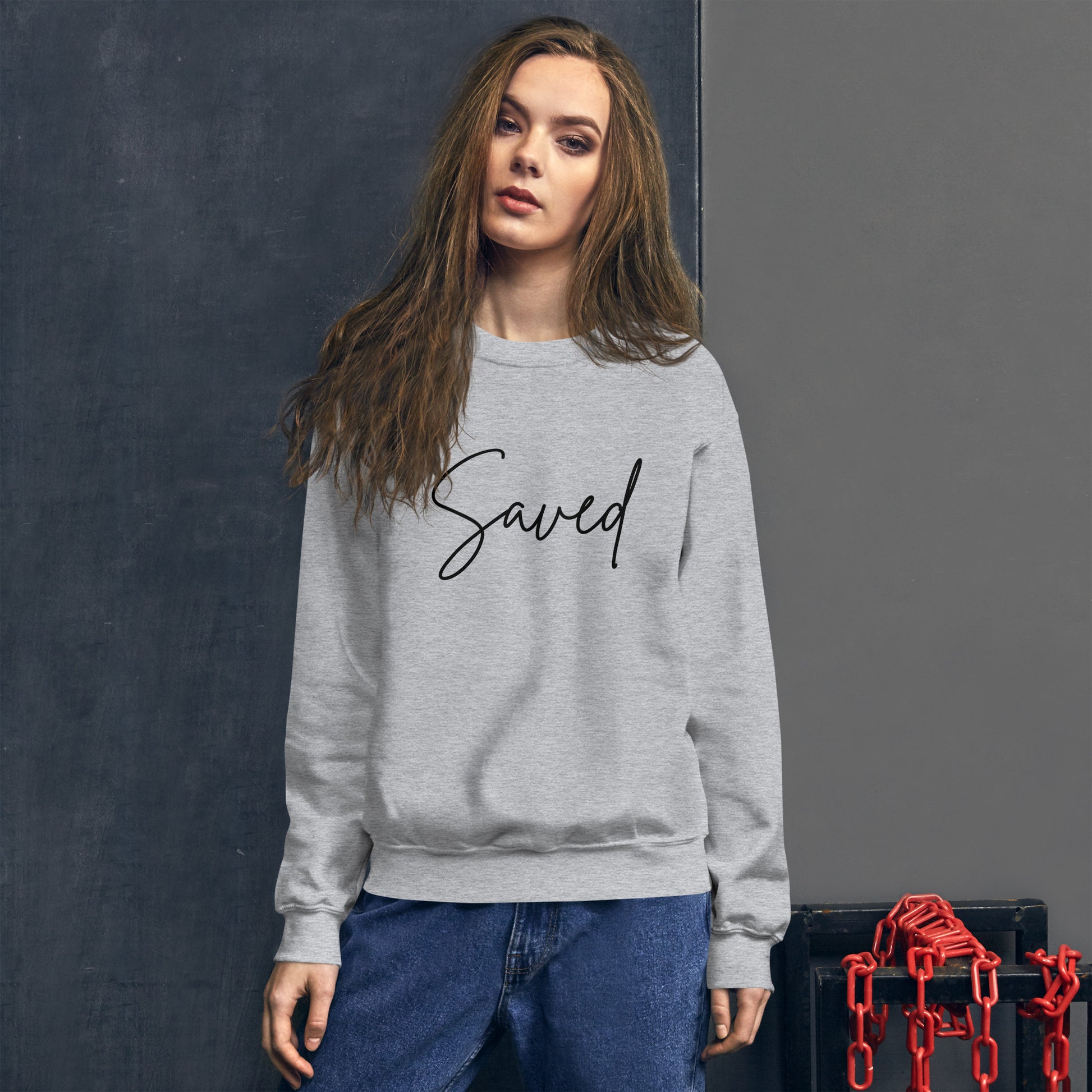Woman wearing sport grey Saved crewneck sweatshirt, front design visible while walking outdoors with a relaxed vibe
