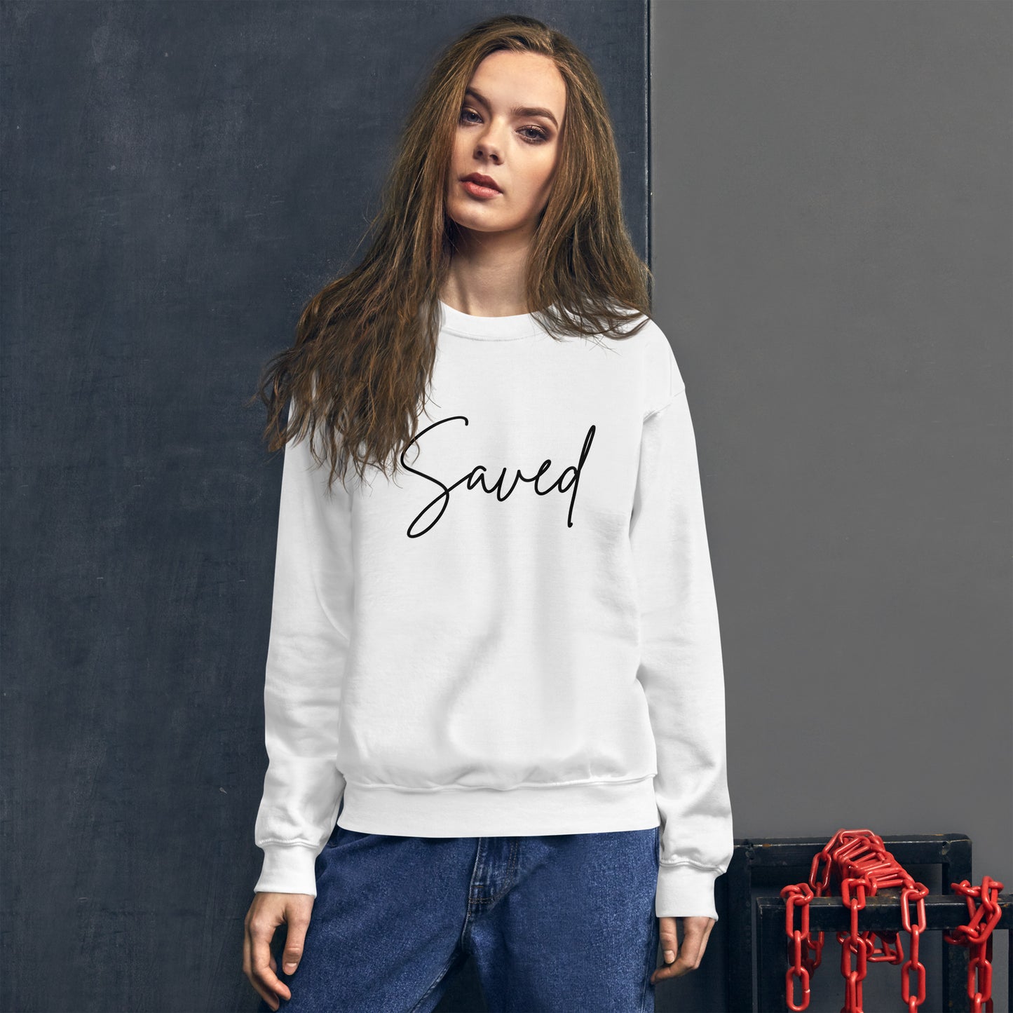 Woman smiling while wearing white Saved crewneck sweatshirt, front design clearly visible in casual outdoor setting
