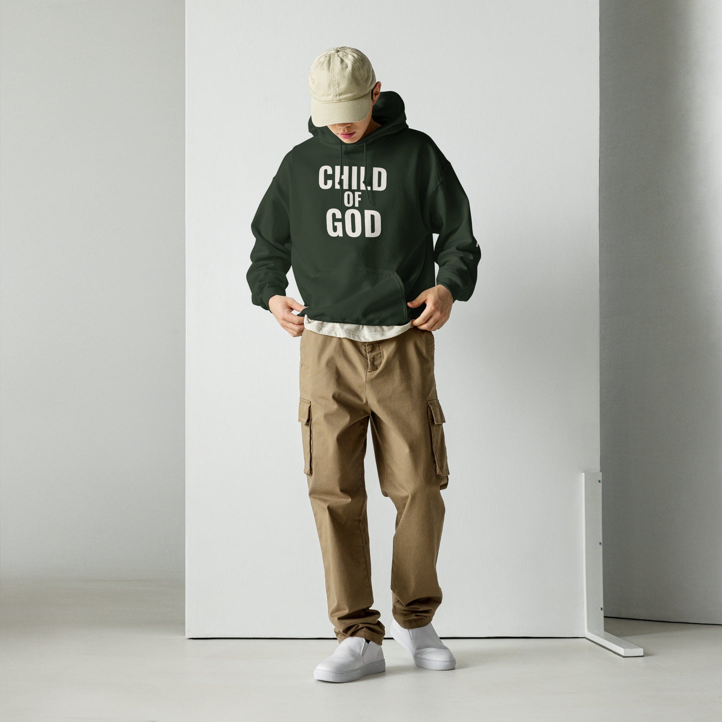 Man wearing forest green Child of God hoodie paired with hat and cargo pants for casual Christian apparel look