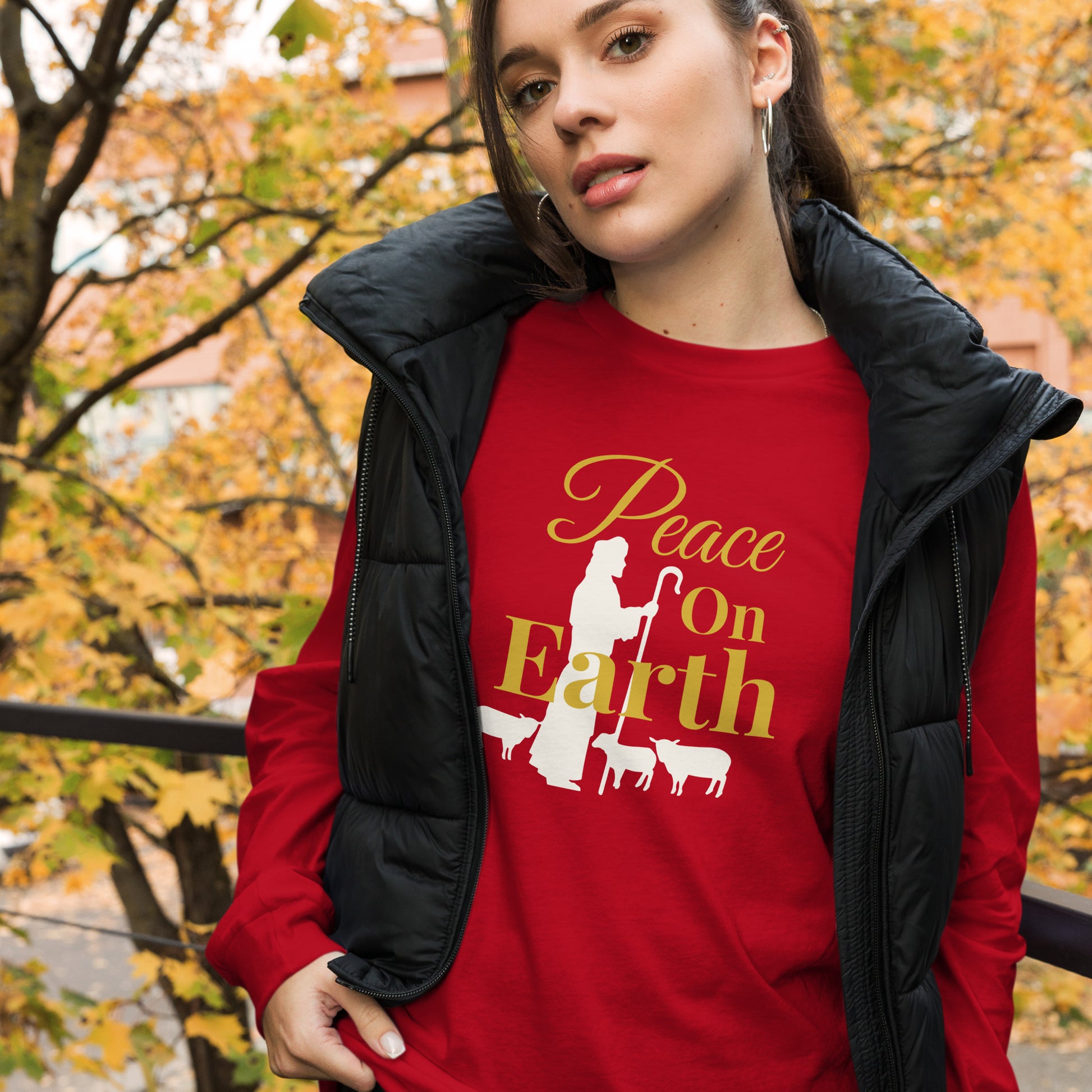 Woman in red Peace on Earth long sleeve Christmas tee with shepherd and sheep graphic, layered with vest
