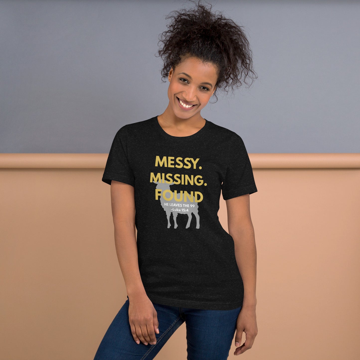 Woman wearing “Messy. Missing. Found.” Christian tee in black heather, standing outdoors, front design with yellow lettering and lamb silhouette visible
