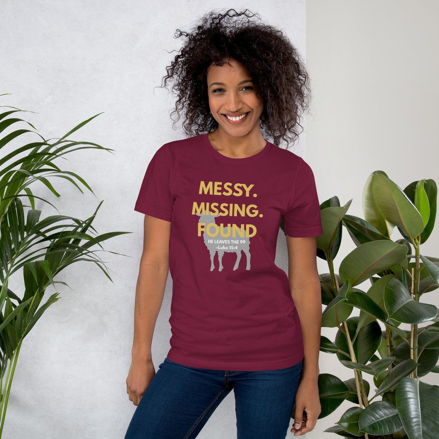 Female model wearing maroon “Messy. Missing. Found.” tee outdoors, front view showing bright yellow design and scripture reference Luke 15:4
