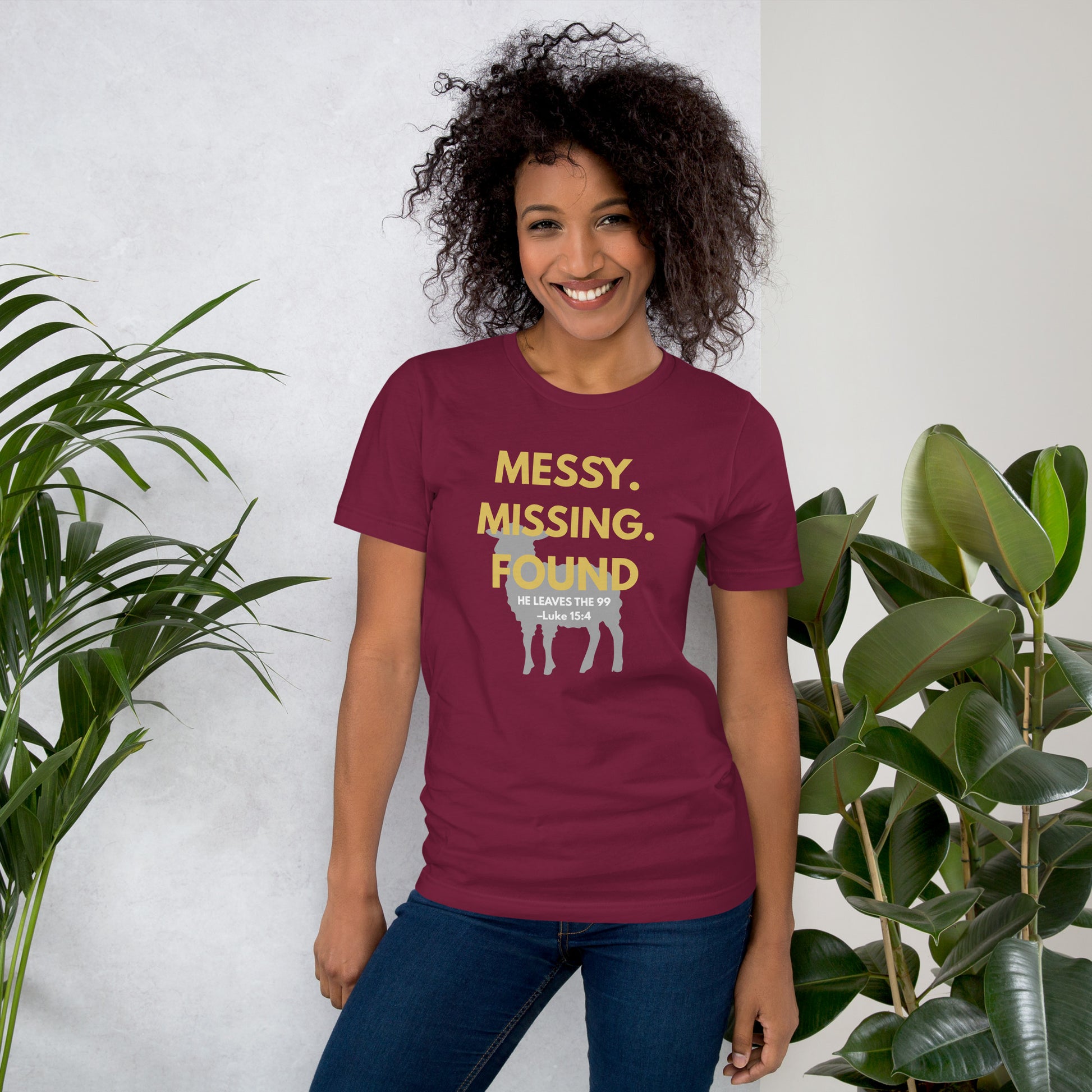 Female model wearing maroon “Messy. Missing. Found.” tee outdoors, front view showing bright yellow design and scripture reference Luke 15:4
