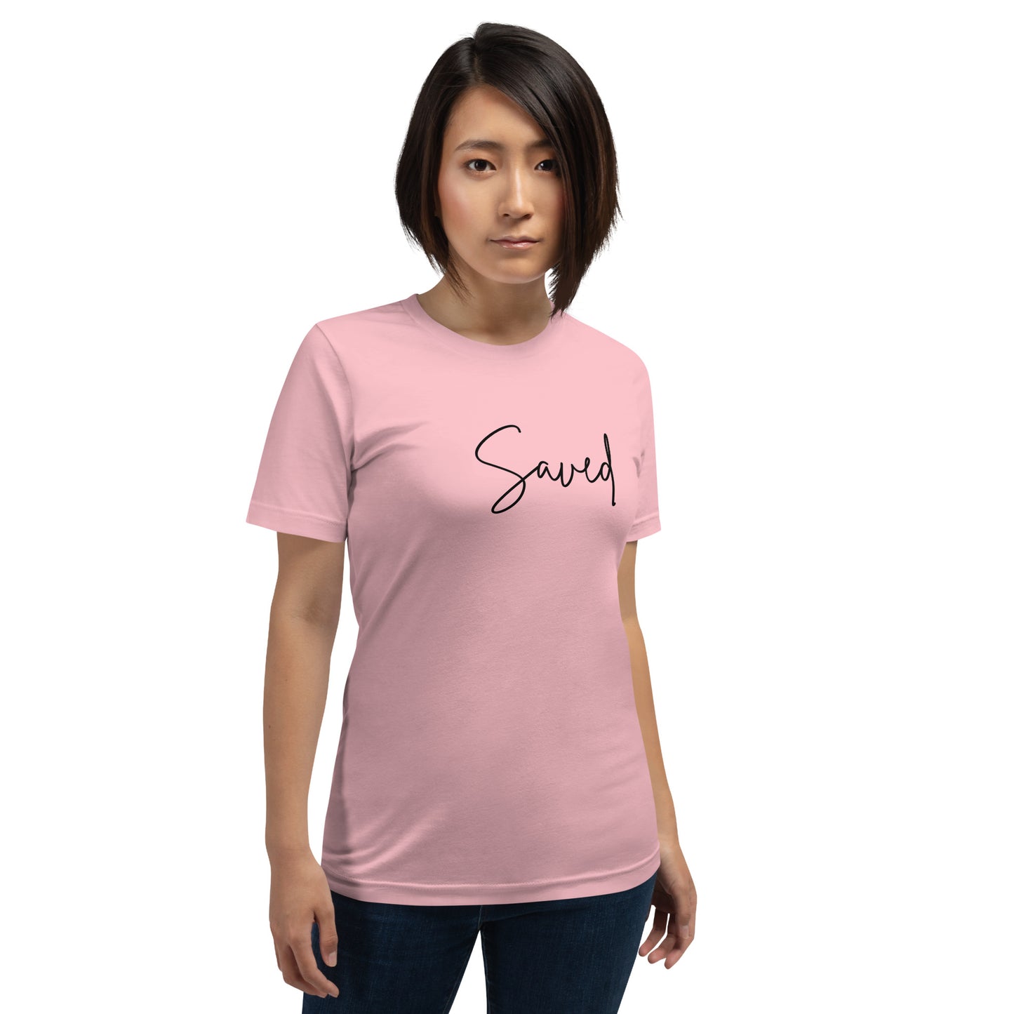 Female model wearing pink “Saved” script tee outdoors, smiling with front design clearly visible
