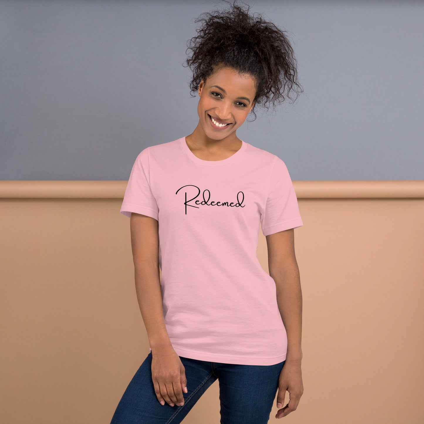 woman wearing the Redeemed Tee in pink, standing front-facing and smiling  