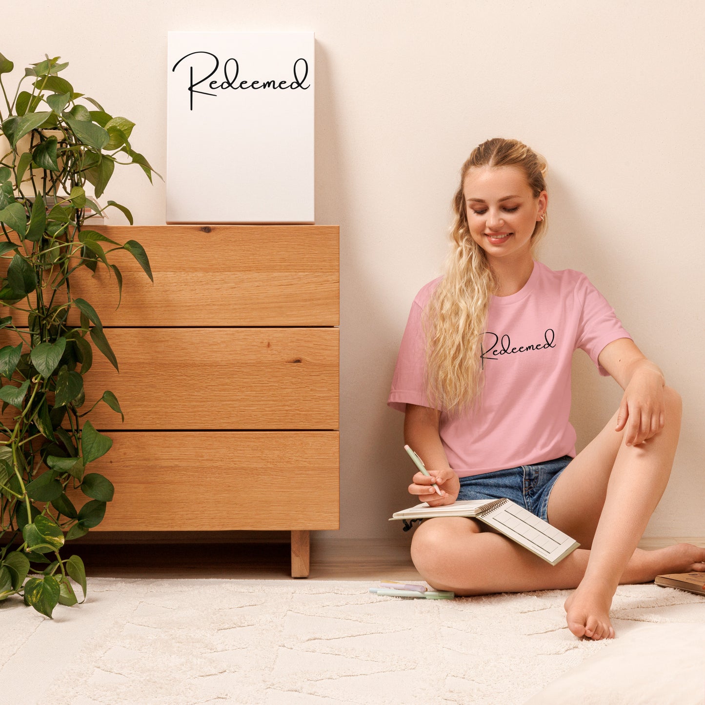 woman modeling the Redeemed Tee in pink, seated with relaxed front view pose