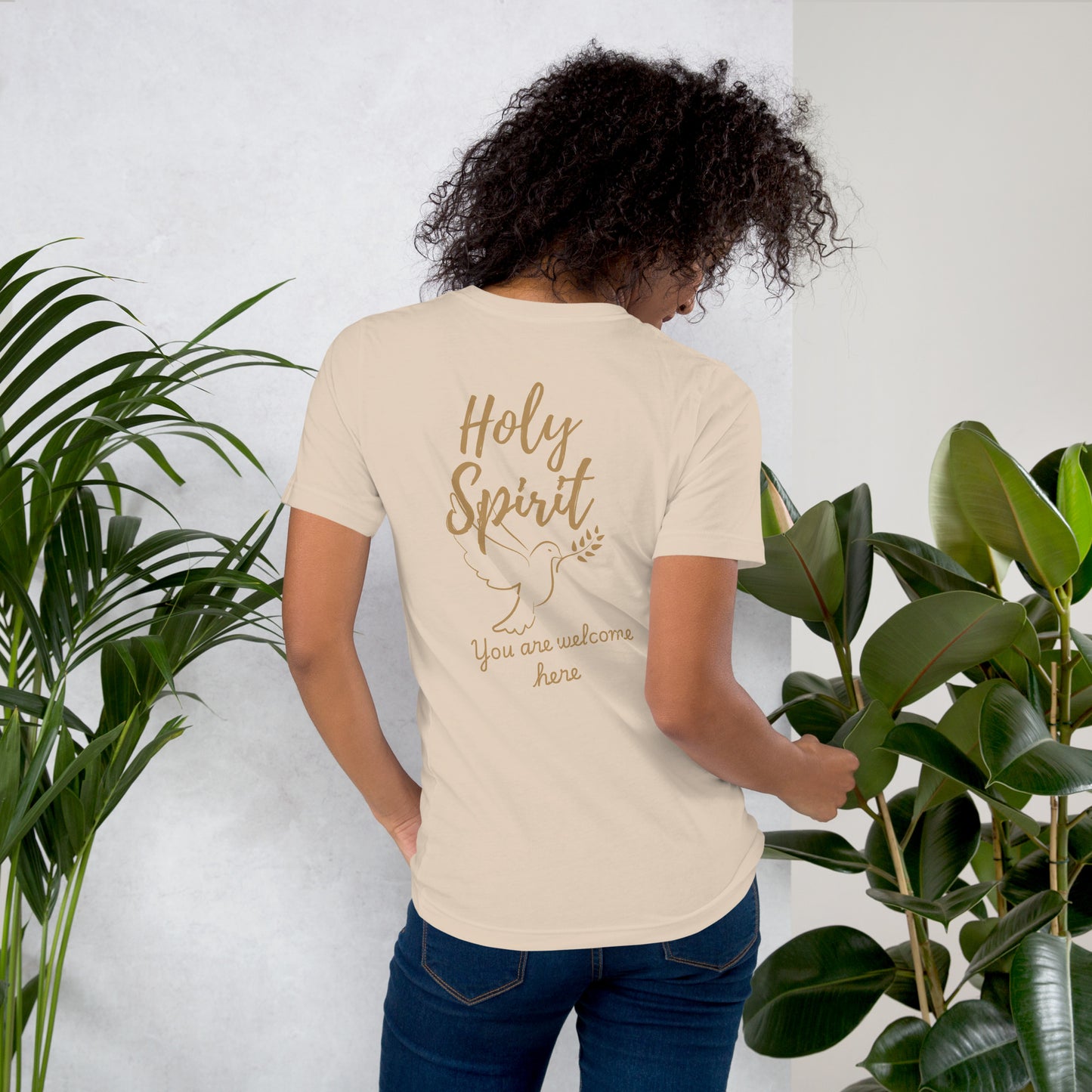 Female model wearing cream-colored Holy Spirit t-shirt, back view with large “Holy Spirit” text, dove graphic, and “You Are Welcome Here” script – gospel-inspired apparel

