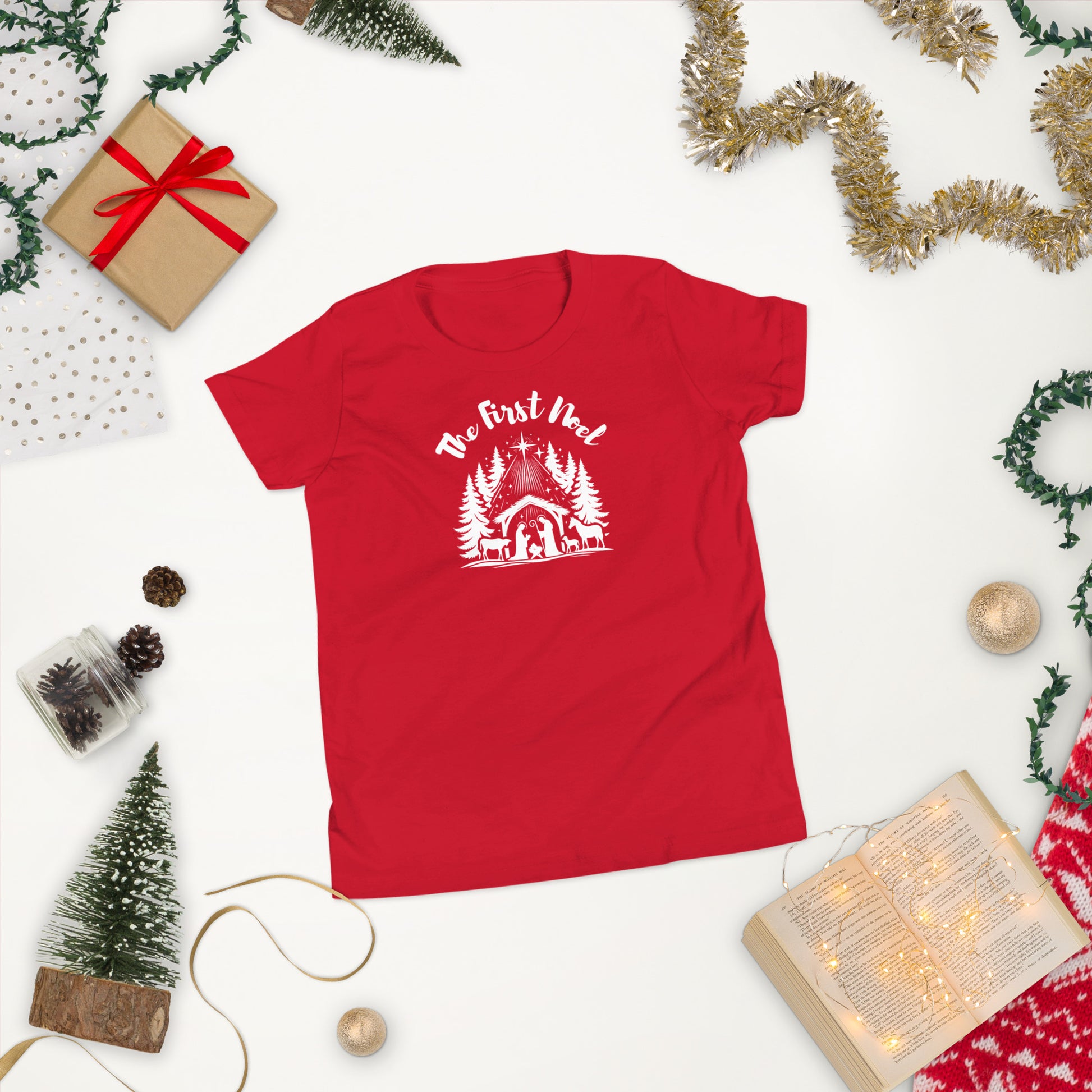 Youth red Christian Christmas tee with white nativity design and The First Noel text inspired by Luke 2:11, in a christmas scene

